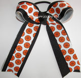 A cheerleader hair bow featuring a white ribbon printed with orange basketballs and black borders, tied into a large bow with long tails, shown on a plain white background.
